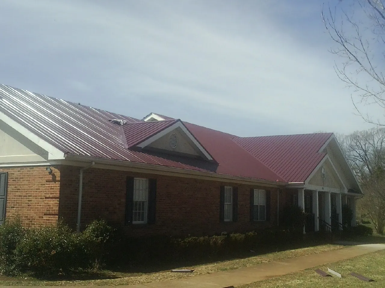 Red metal roof with gabled entries on a long brick building, from a Hail Damage Roof Repair job in Hurricane