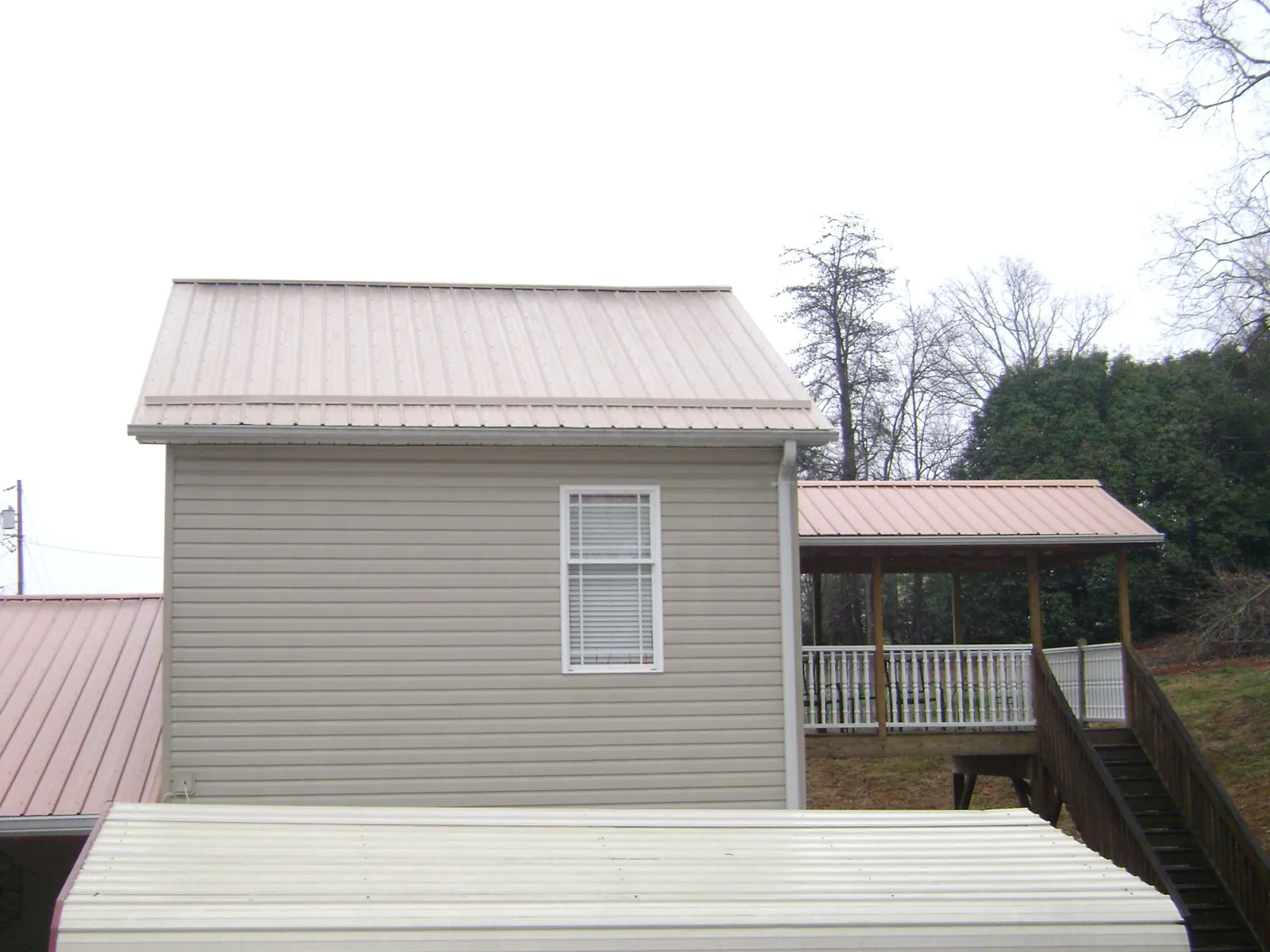 Tan metal roofs on a two story addition and attached porch, from a Roof Replacement job in Hurricane